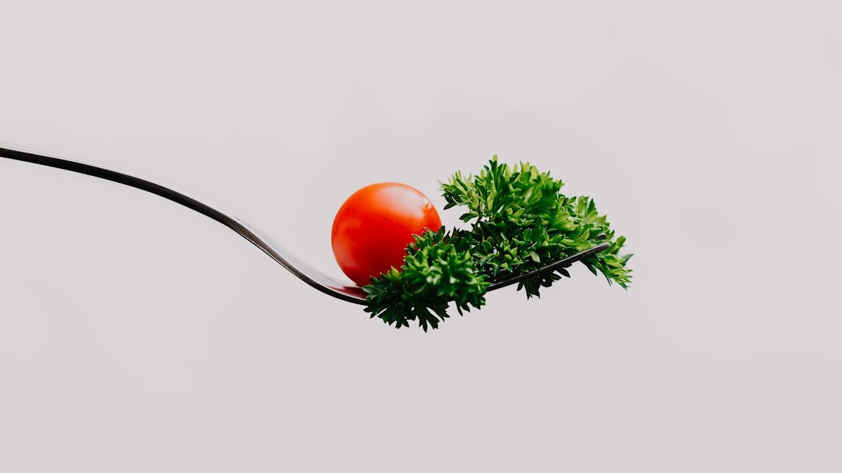 Minimalist close-up of a cherry tomato and parsley on a fork. Perfect for food design.